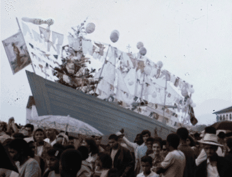 Gif animado com cenas do filme O Mastro do Bino Santo (1971). Na primeira cena, vê-se o barco Palermo com bandeira hasteada levando a imagem de São Benedito; em seguida, três homens (dois sem camisa e um, mais ao fundo, de chapéu) estão no chão puxando o barco.