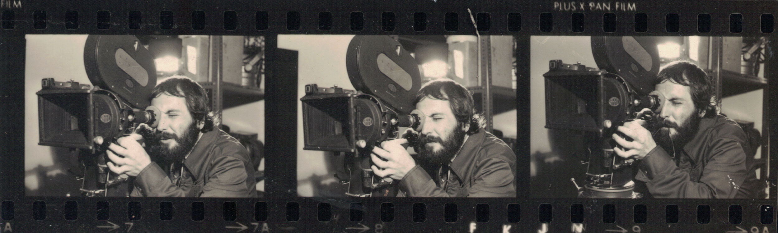 Trecho de negativo de imagem no qual Ramon Alvarado opera câmera cinematográfica e olha através de seu visor. Imagem preto e branco. Fotógrafo(a) não identificado(a).